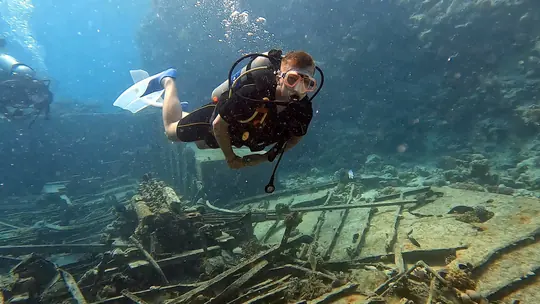 Scuba diver holding a horizontal trim above a wreck, illustrating Peak Performance Buoyancy