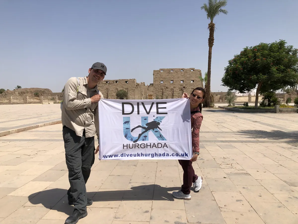 Two guests holding a Dive UK Hurghada flag in front of an Egyptian temple
