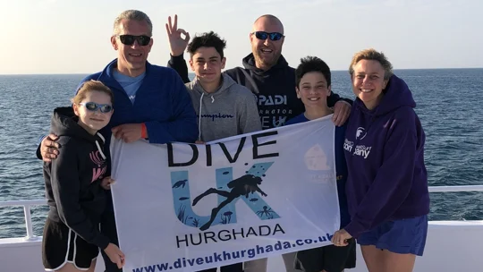 Adults and children holding the Dive UK Hurghada flag on a Red Sea boat day