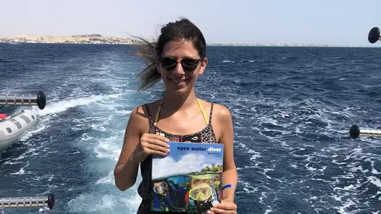 Diver holding a PADI Open Water Diver manual on a boat