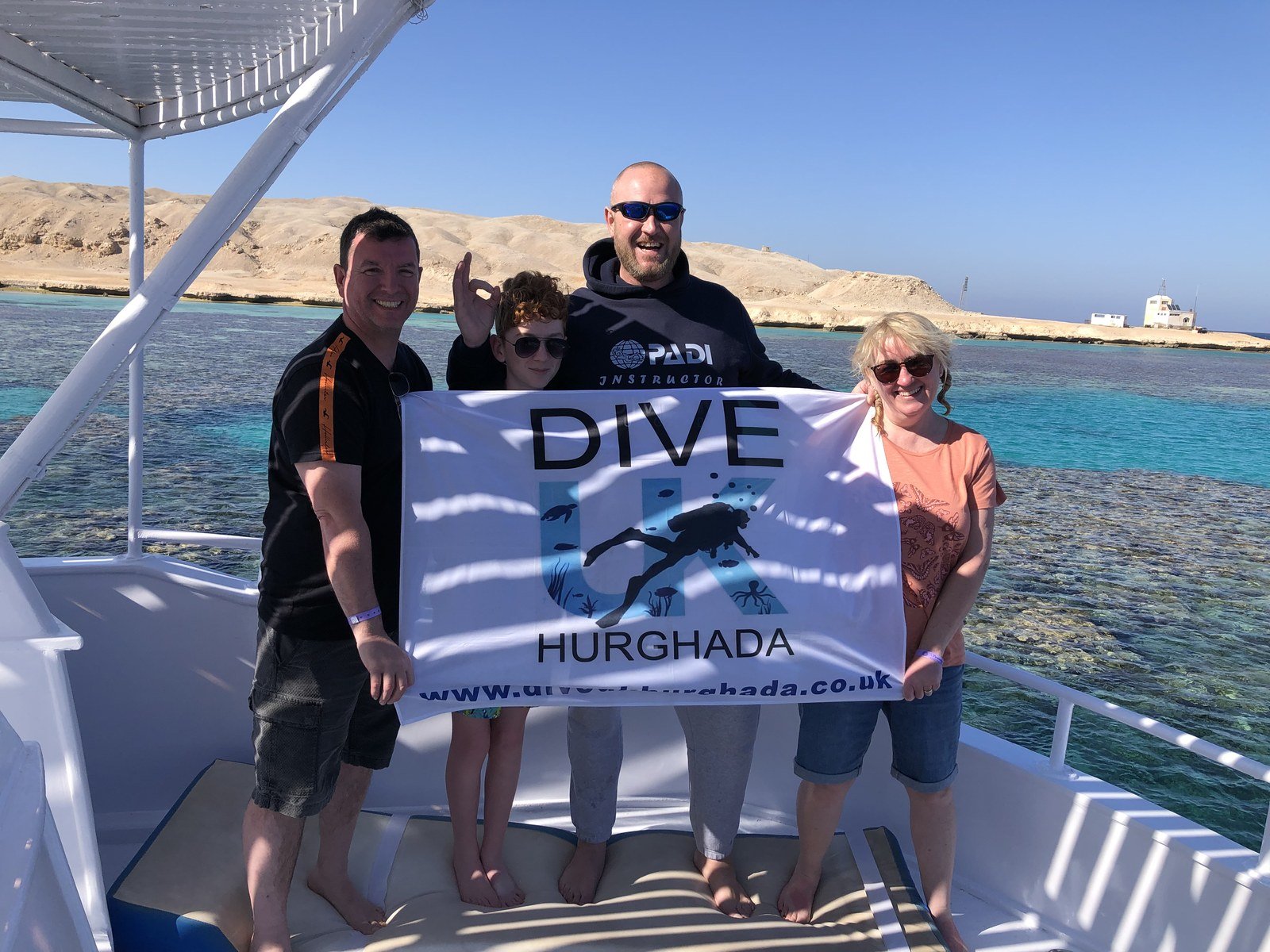Four people holding a Dive UK Hurghada flag on a boat