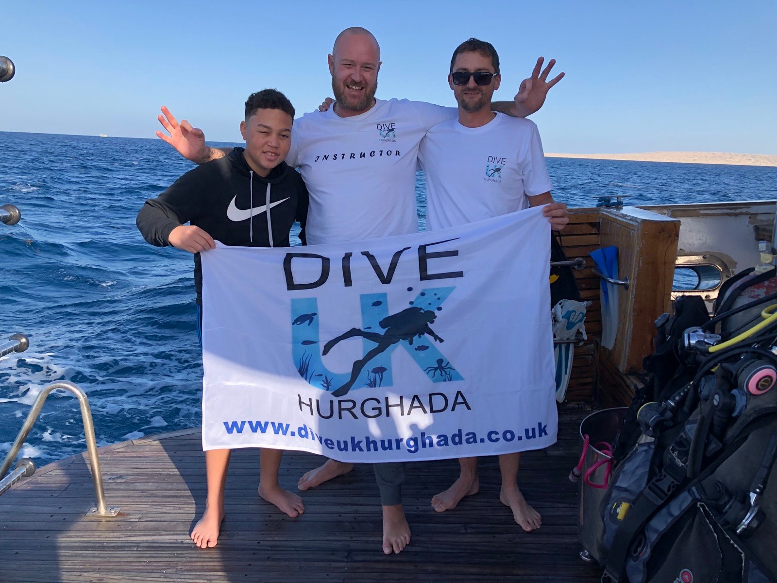 Dive UK Hurghada instructor and guests holding the company banner on a dive boat