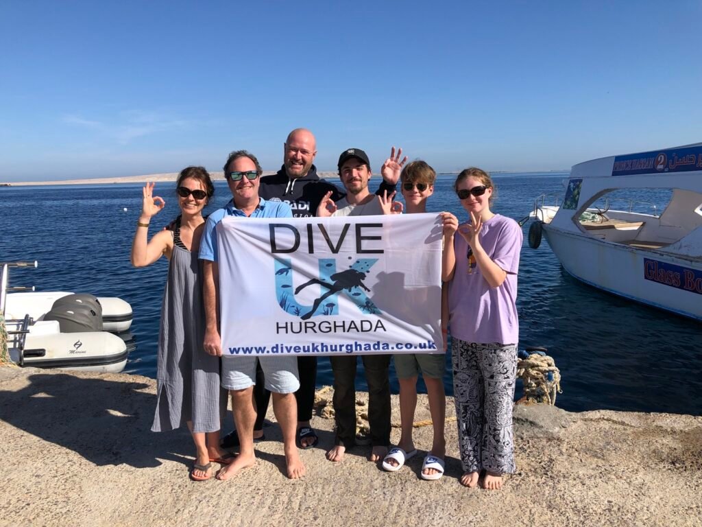 Group holding the Dive UK Hurghada flag beside the Red Sea