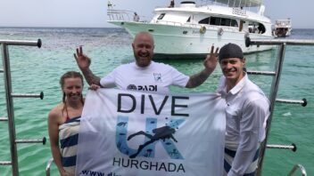 Dive UK Hurghada guests holding our flag beside the turquoise Red Sea