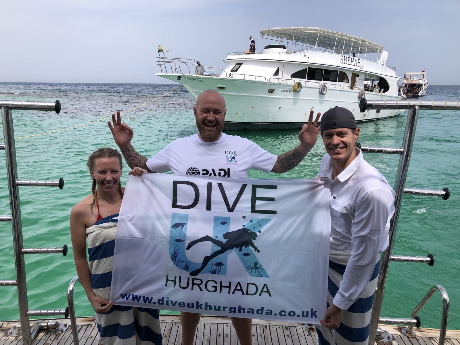 Dive UK Hurghada guests holding our flag beside the turquoise Red Sea