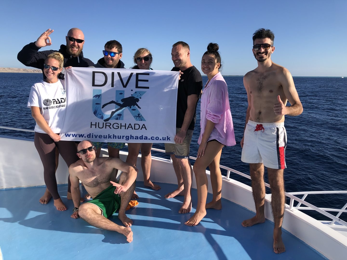 Guests holding the Dive UK Hurghada flag on the dive boat