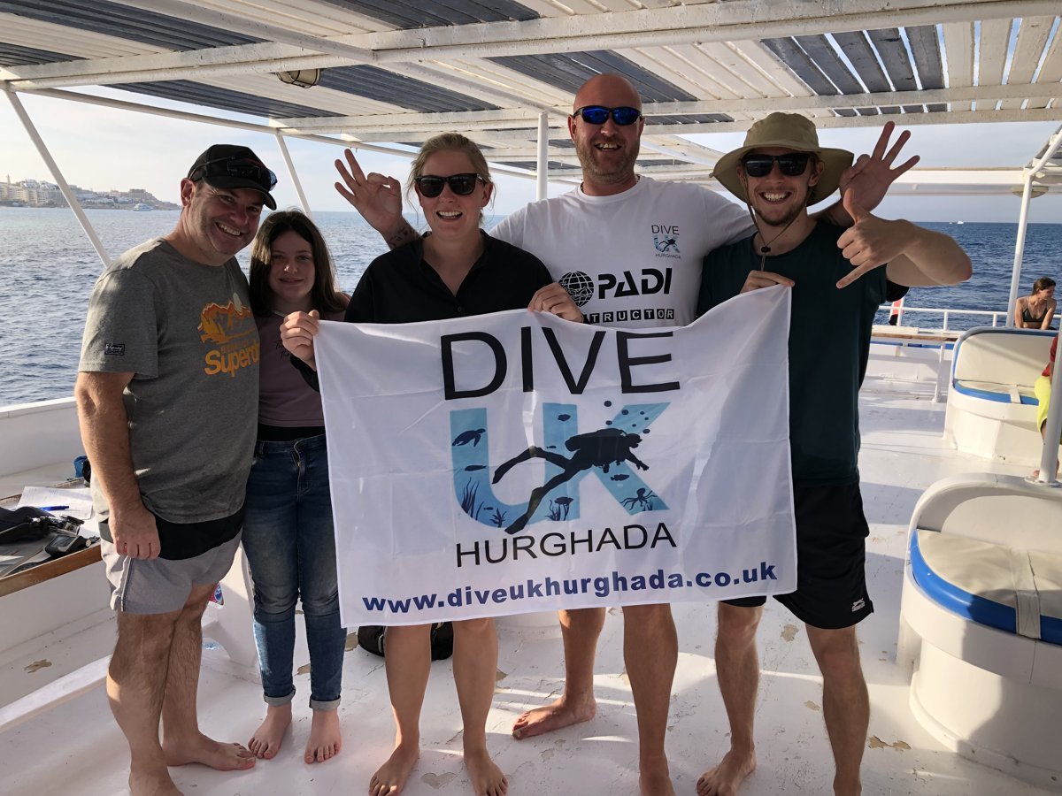 Guests holding the Dive UK Hurghada flag together on the boat