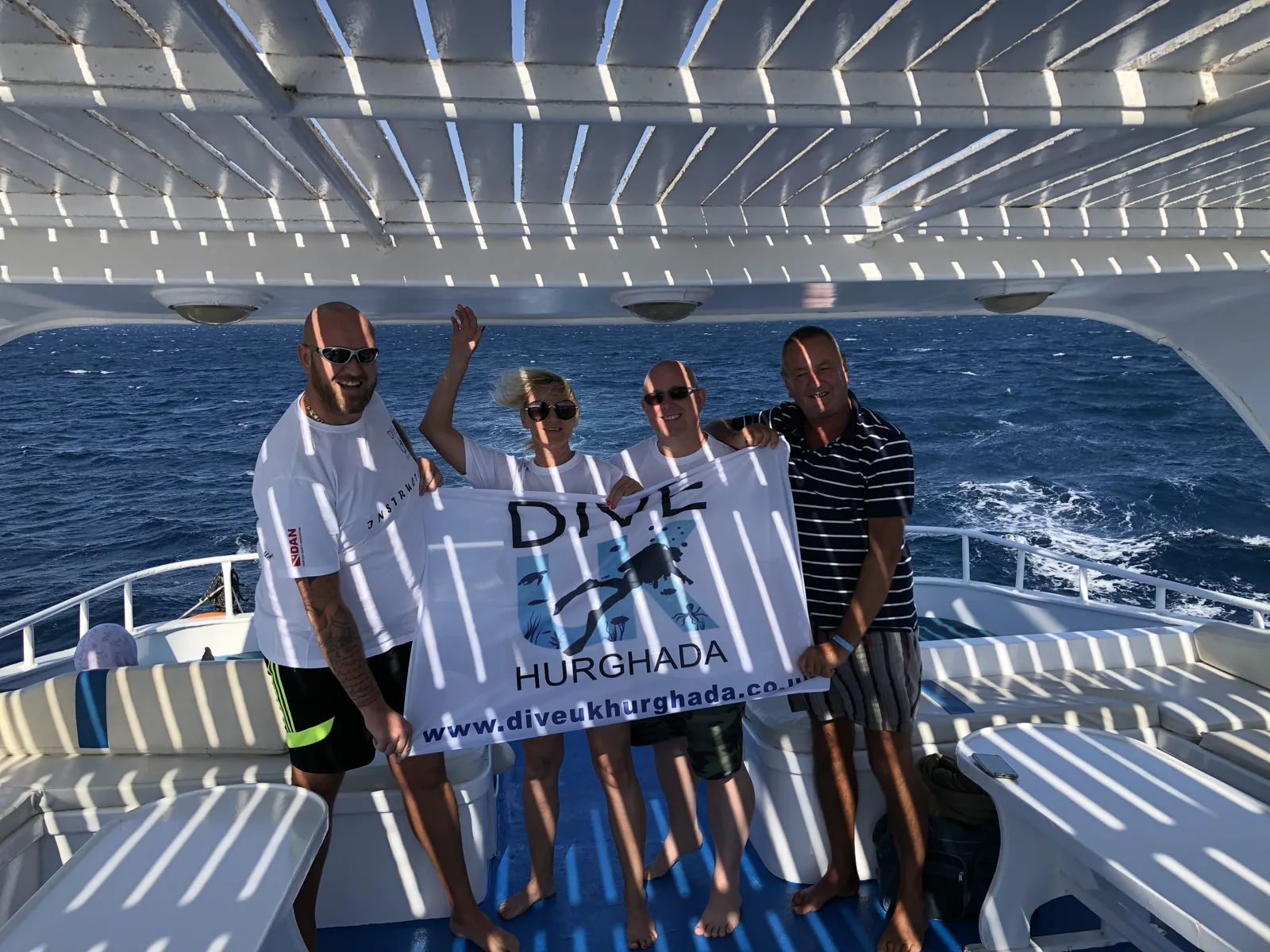 Four guests holding a Dive UK Hurghada flag on the dive boat