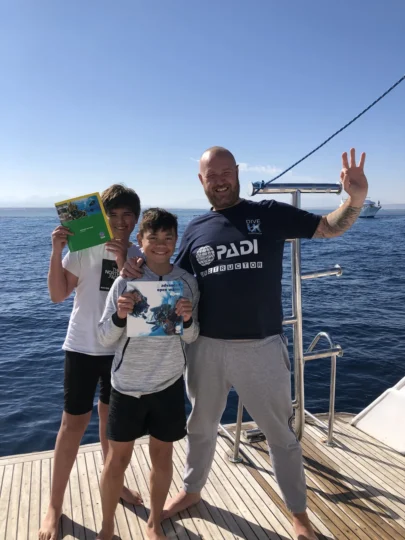 Two young divers with course books and their instructor, showing the Junior Advanced diving journey in Hurghada