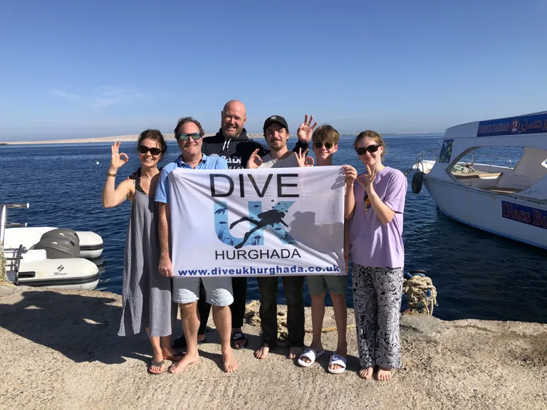 Guests holding a Dive UK Hurghada flag beside the sea