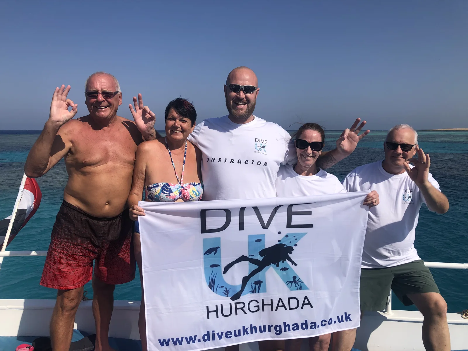 Dive UK Hurghada guests holding the team banner on a boat in the Red Sea